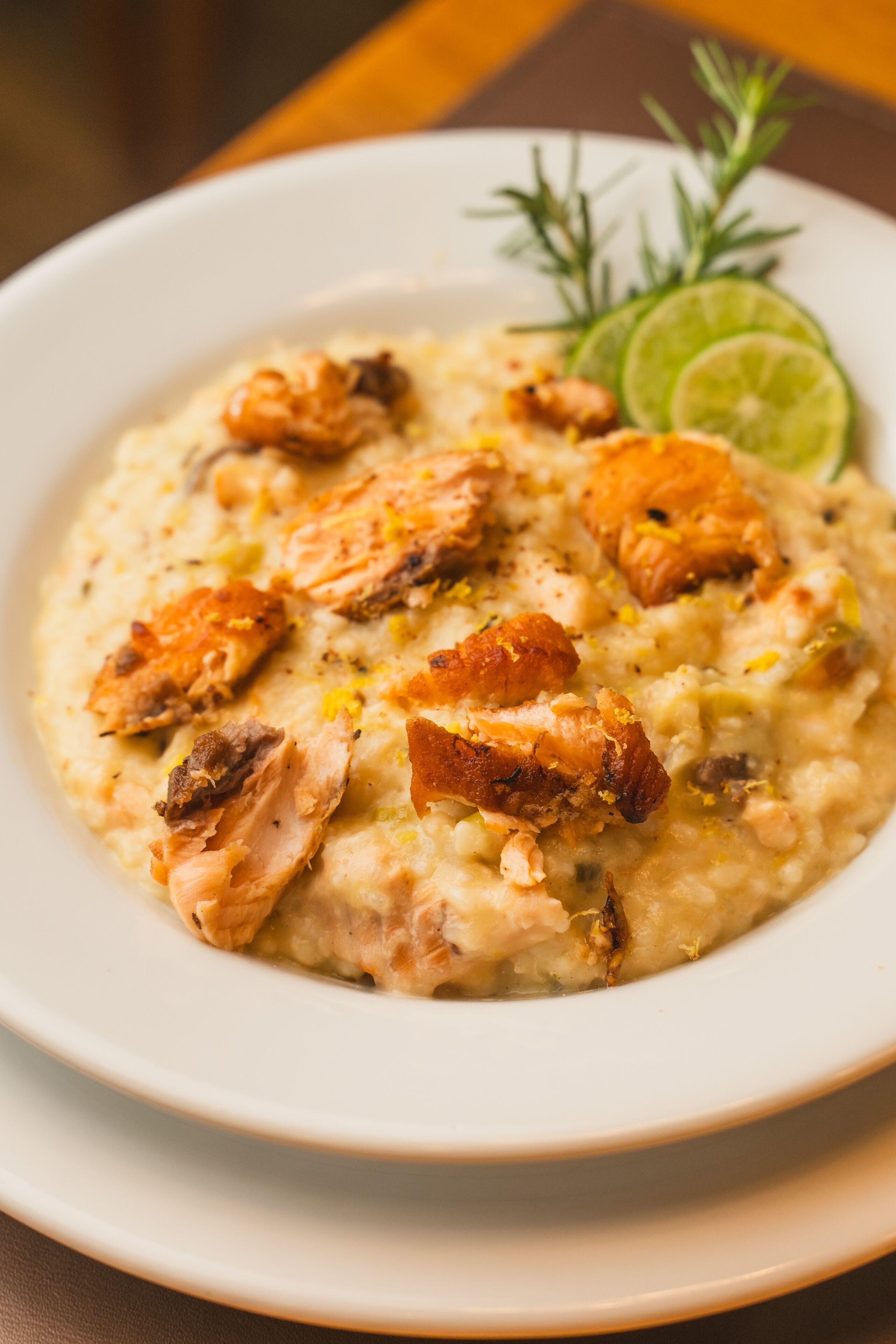 A plate of creamy risotto with salmon and garnished with lime and rosemary.