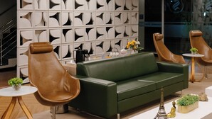 A modern lobby with a green sofa, leather armchairs, a white coffee table, and decorative items including a model of the Eiffel Tower. -  Strassen Hotel (Aparecida de Goiania)