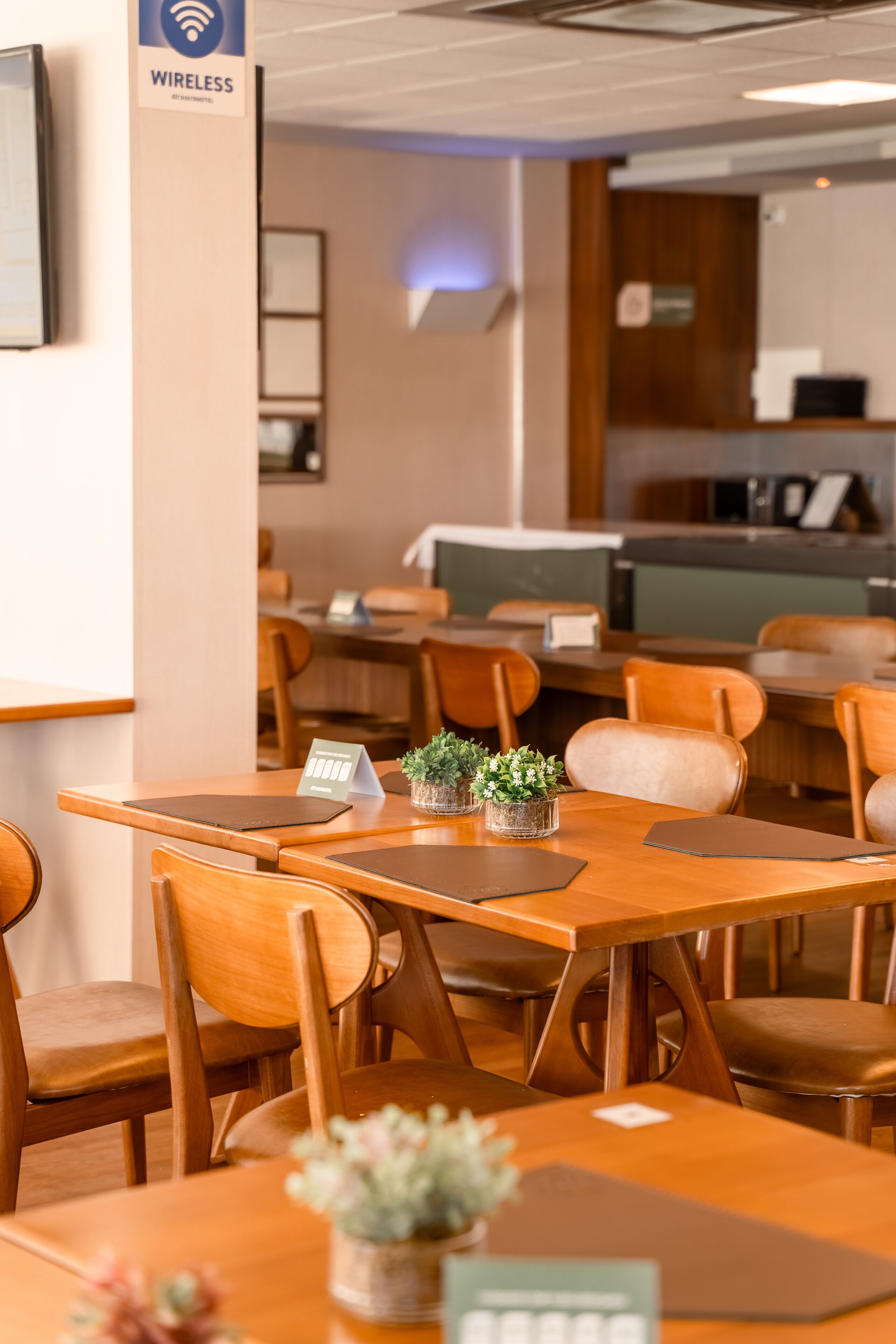 Um restaurante com mesas e cadeiras de madeira, um aviso indicando acesso à rede sem fio e uma pequena planta na mesa.