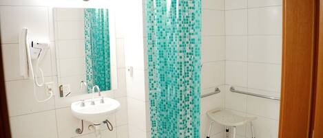 Een badkamer met een wit wastafel, een spiegel, een douche met een turquoise mozaïek gordijn, en een klein wit bankje.