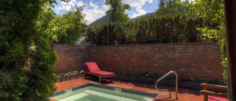 Um quintal com piscina, uma cadeira de lounge vermelha, um banco de madeira e um muro de tijolos.