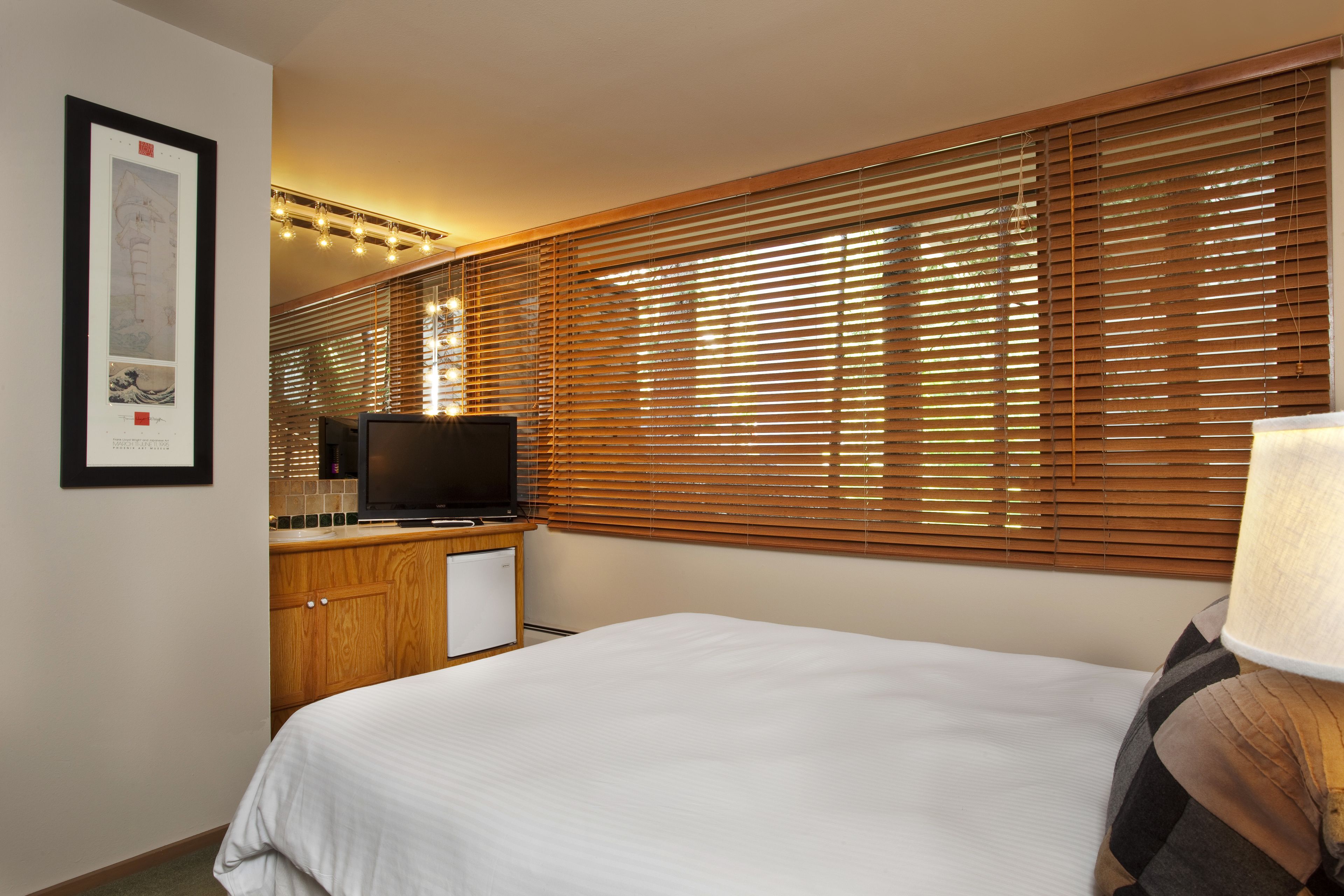 Een hotelkamer met een bed, een televisie, houten jaloezieën en een kleine kitchenette.