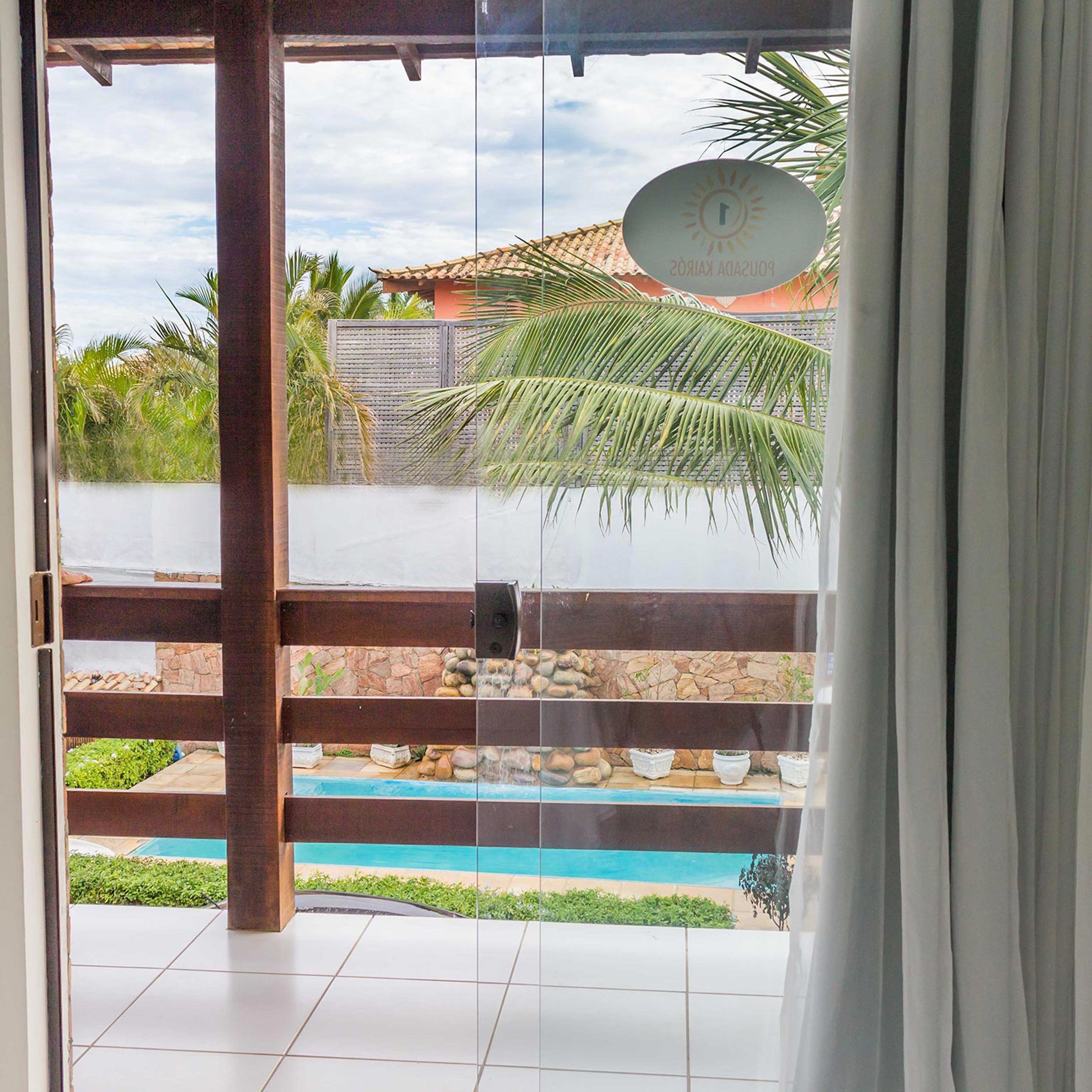 A view through a glass door to a pool area with a tiled floor, a stone wall, and a palm tree.