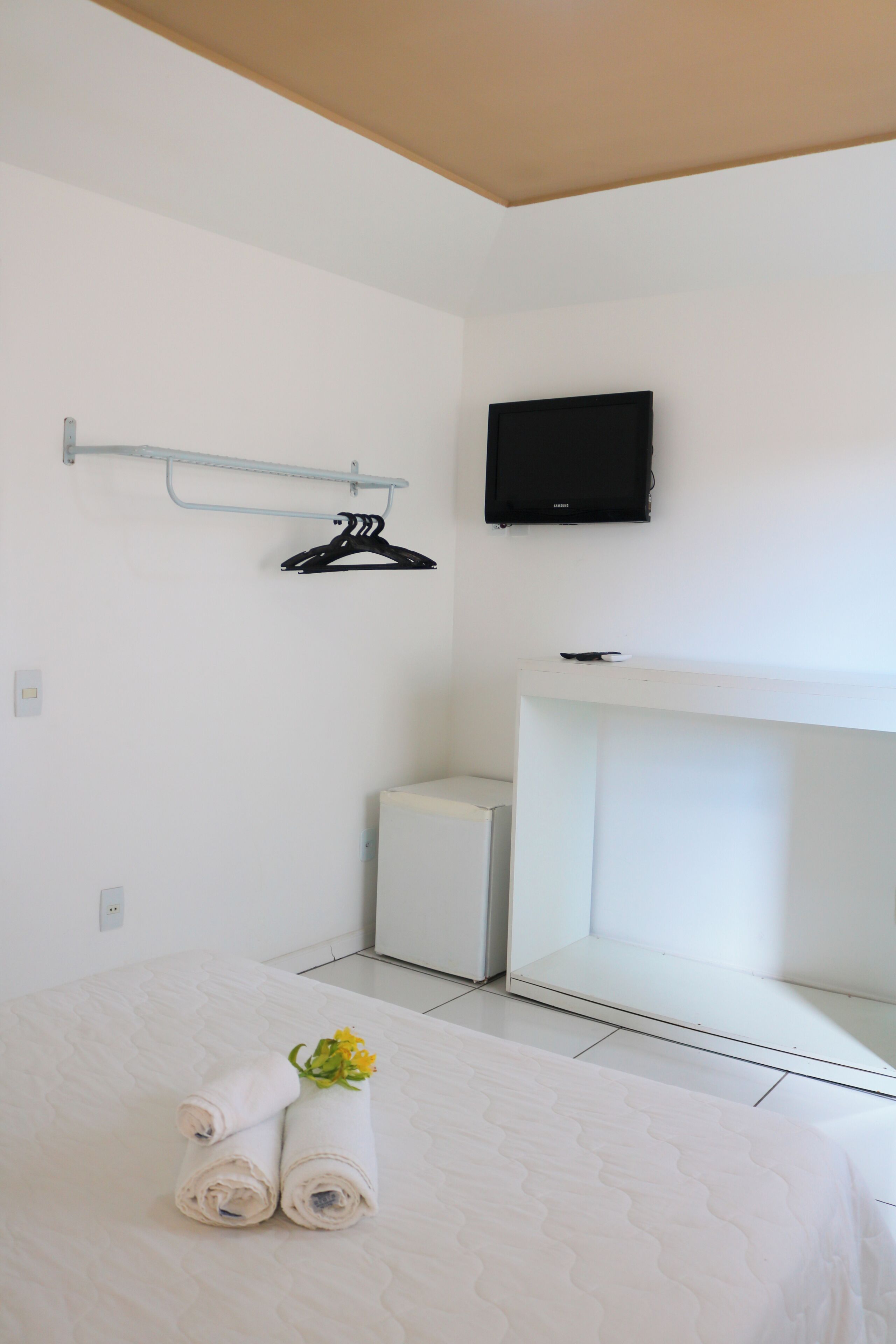 A hotel room with a bed, a TV mounted on the wall, a small desk, and a wall-mounted coat rack.
