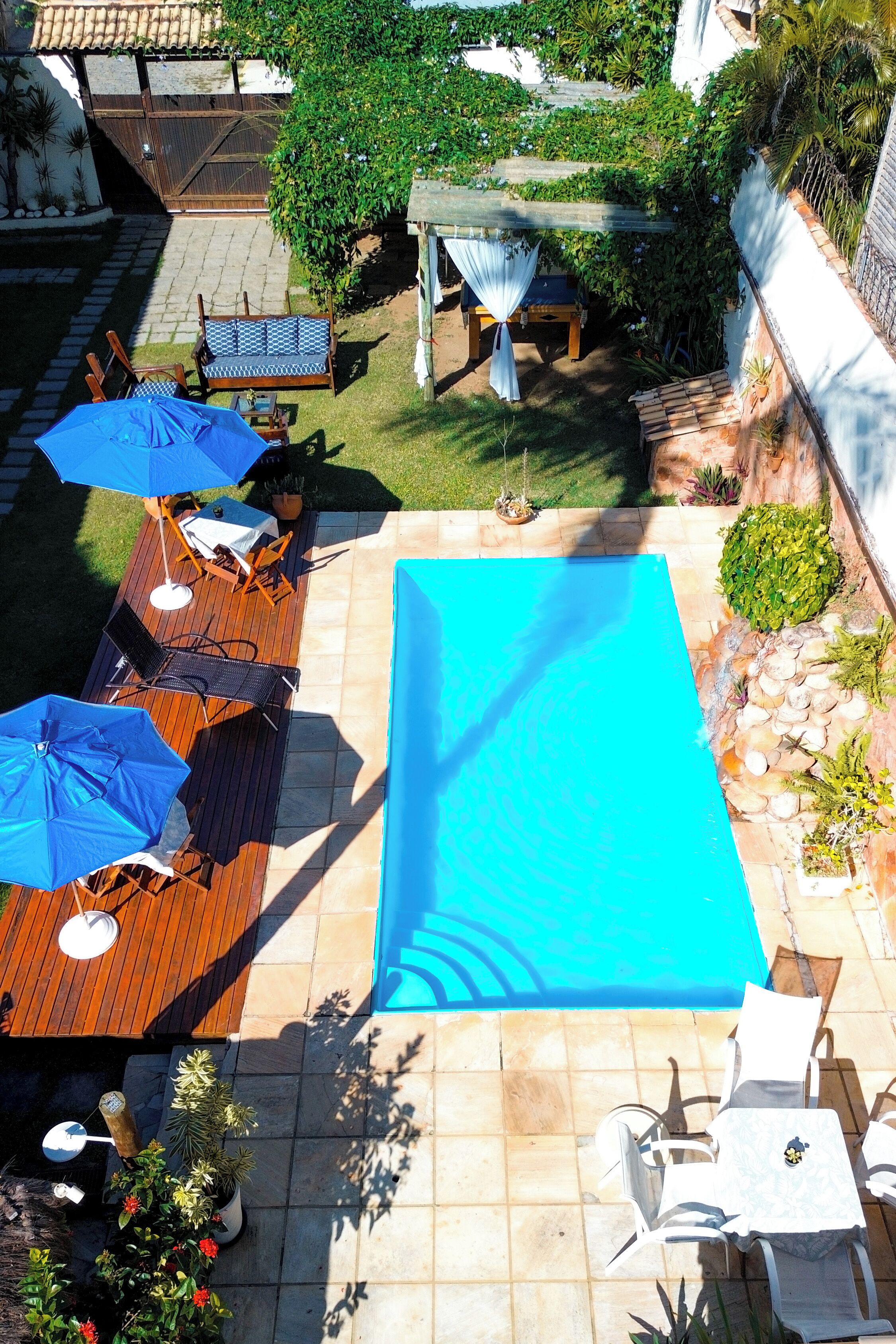 Piscina en la azotea con mobiliario de madera, sombrillas y abundante vegetación, además de una pérgola.