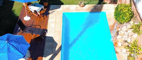 Piscina en la azotea con mobiliario de madera, sombrillas y abundante vegetación, además de una pérgola.