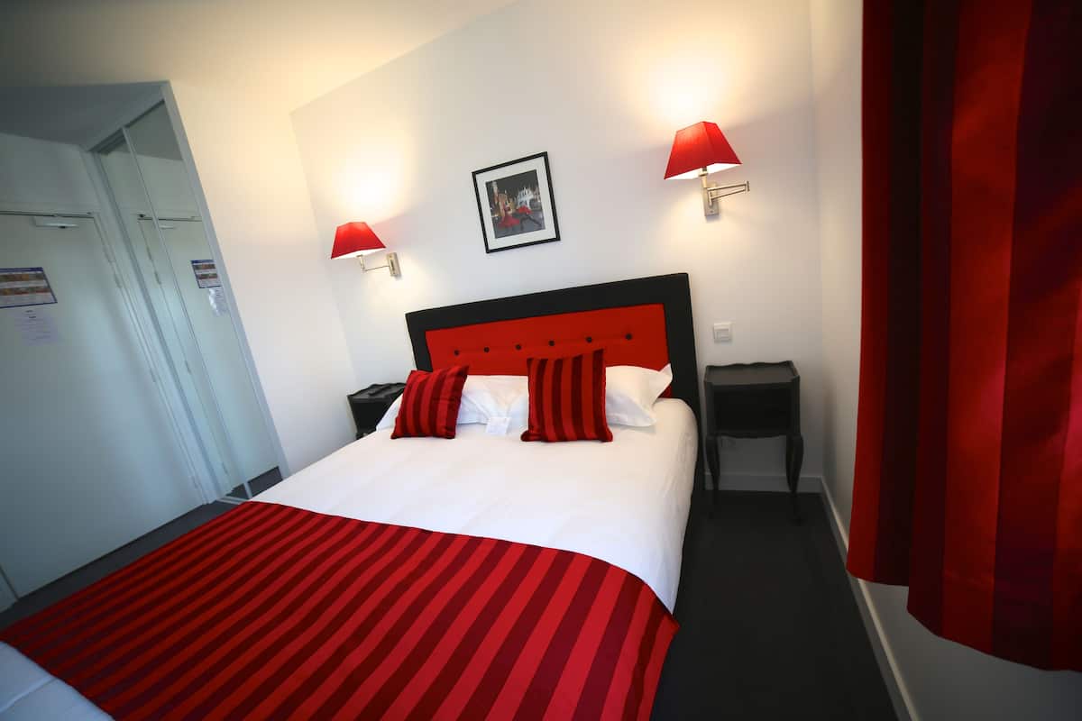 A hotel room with a bed, a nightstand, a red-striped bedspread, and two red wall lamps.