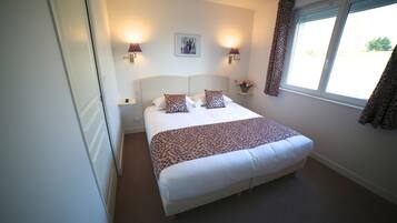 A neatly made bed with a patterned bedspread, two wall-mounted lamps, a framed picture above the bed, and a window with curtains.