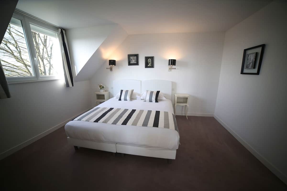 A bedroom with a large bed, two bedside tables, a window, and wall-mounted lights.