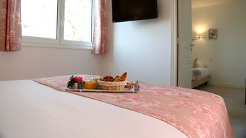 A neatly made bed with a tray of breakfast items, a television mounted on the wall, and a window with curtains.