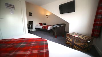 A bedroom with a bed, a desk, a chair, a small table, a TV, and a red plaid blanket.