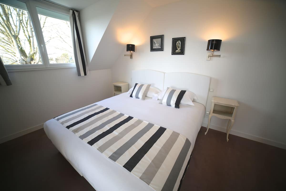 A bedroom with a large bed, two bedside tables, and a window with curtains.