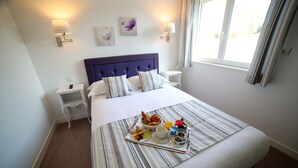 Habitación de hotel con una cama grande, una mesita de noche, una bandeja con desayuno y lámparas de pared.