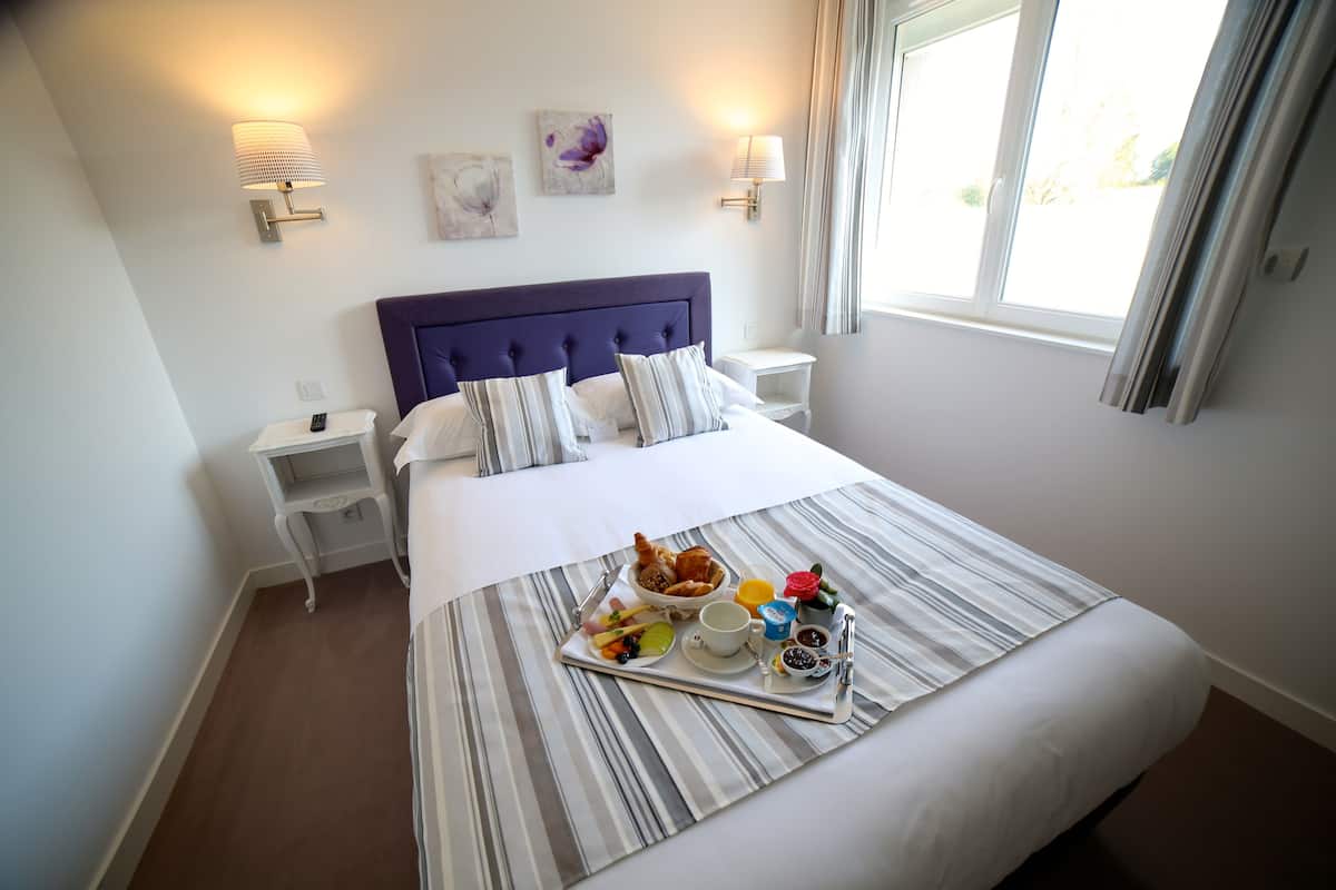 A hotel room with a large bed, a bedside table, a tray with breakfast, and wall-mounted lamps.