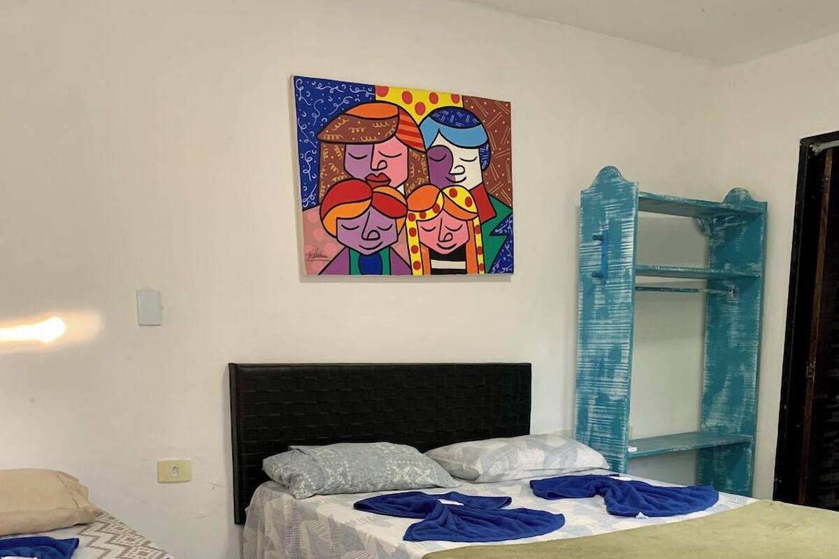 Un dormitorio con dos camas, un cuadro de colores en la pared y un espejo con marco azul.