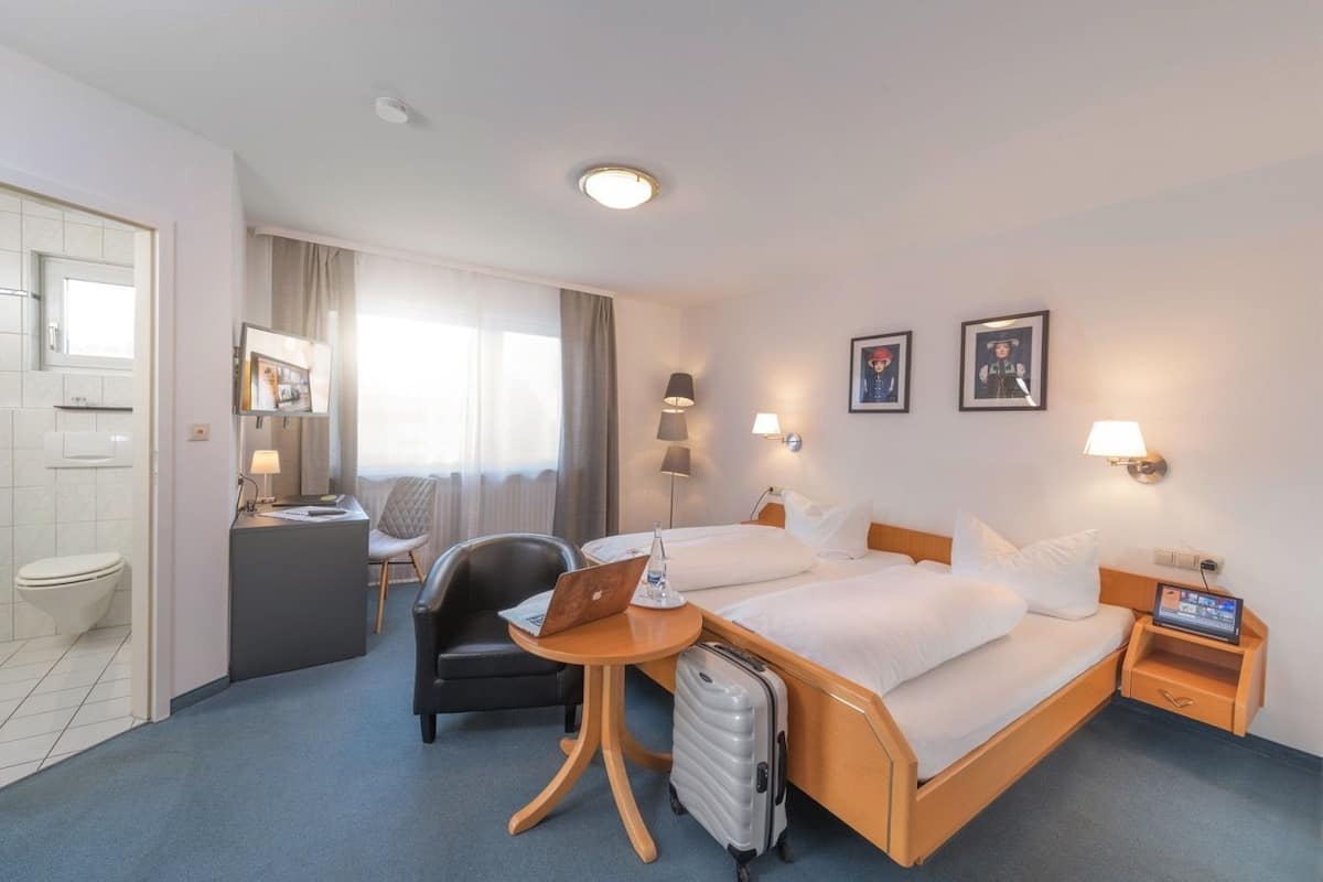 Une chambre d’hôtel avec un lit, un bureau, une chaise et une valise.