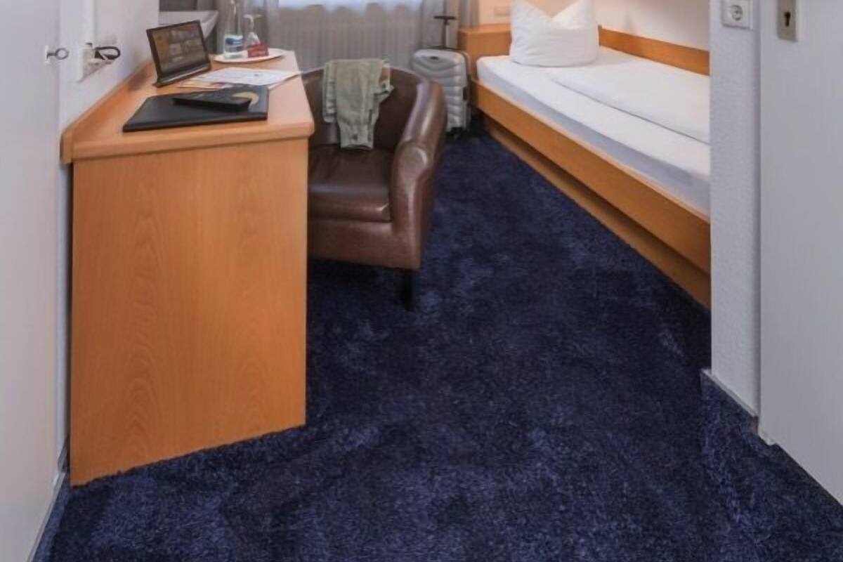 Une chambre d’hôtel avec un lit, un bureau, une chaise, une lampe et une fenêtre avec des rideaux.
