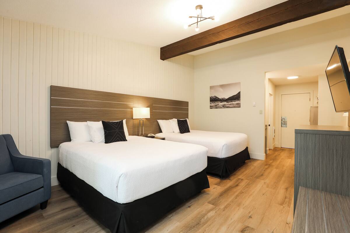 A hotel room with two beds, a desk, a chair, and a mounted TV.