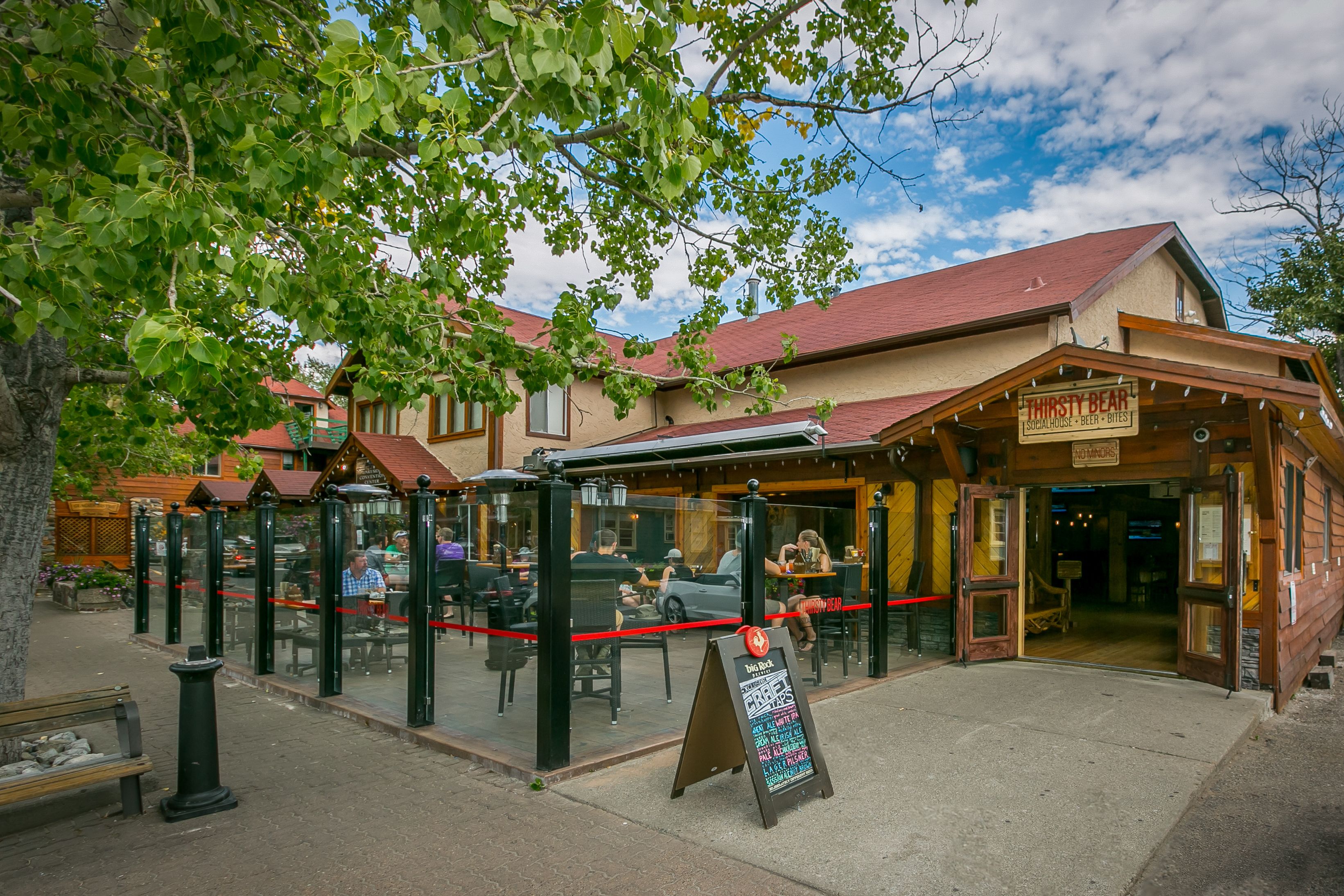A restaurant with outdoor seating, a red rope barrier, and a signboard.