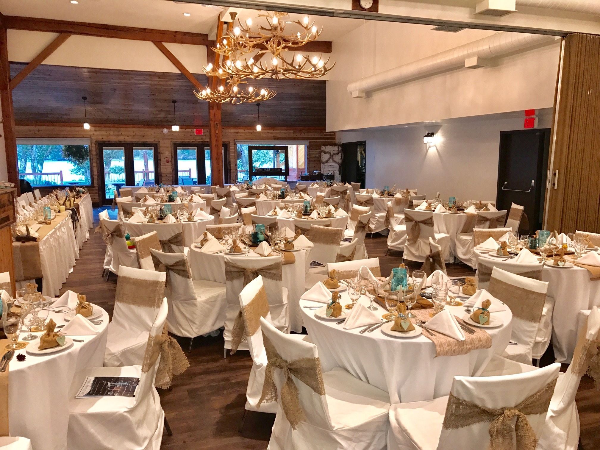Een balzaal met ronde tafels gedekt voor een formeel evenement, met witte tafelkleden en linnen linten.