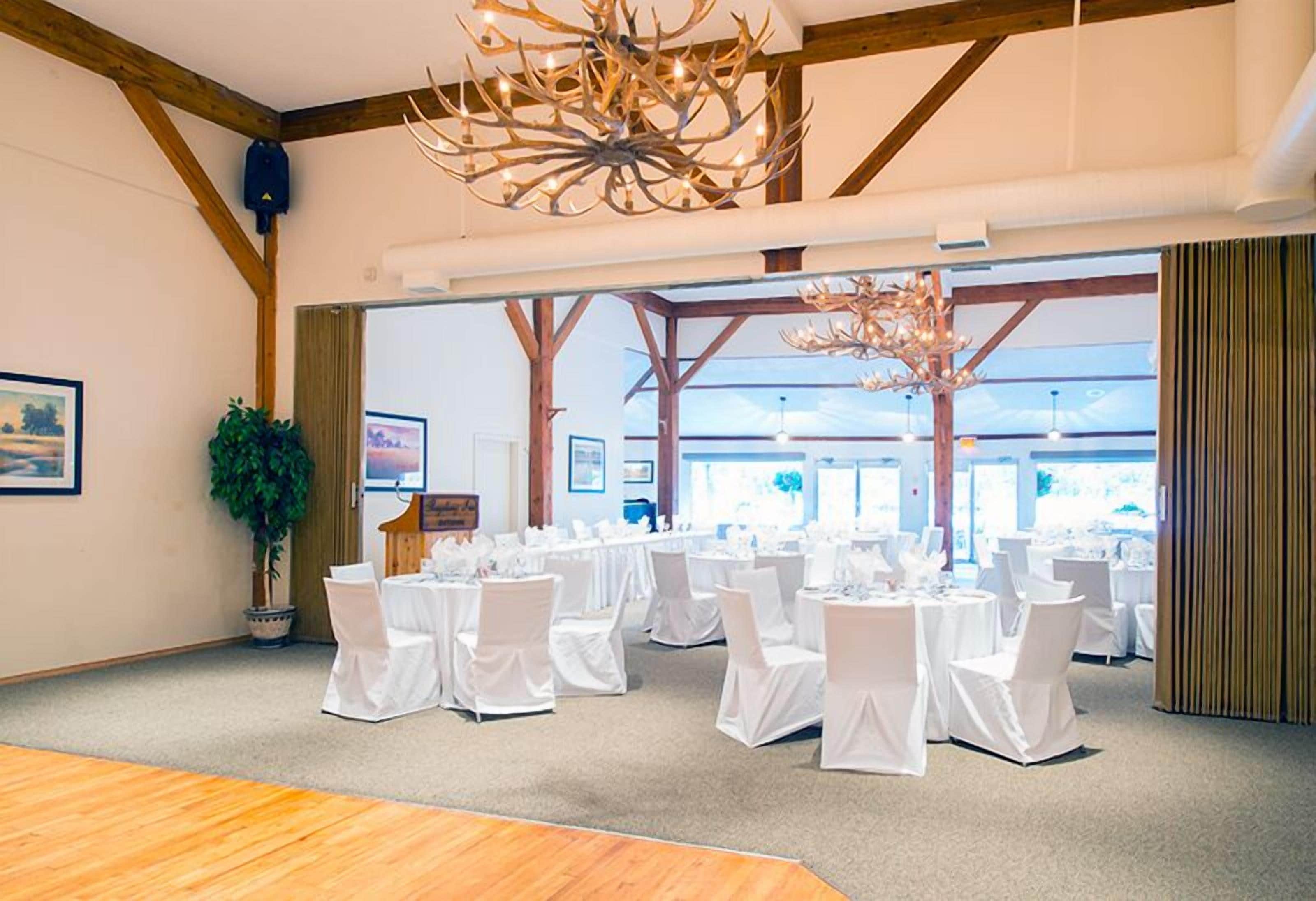 A conference room with white chairs and tables, wooden beams, and a chandelier.