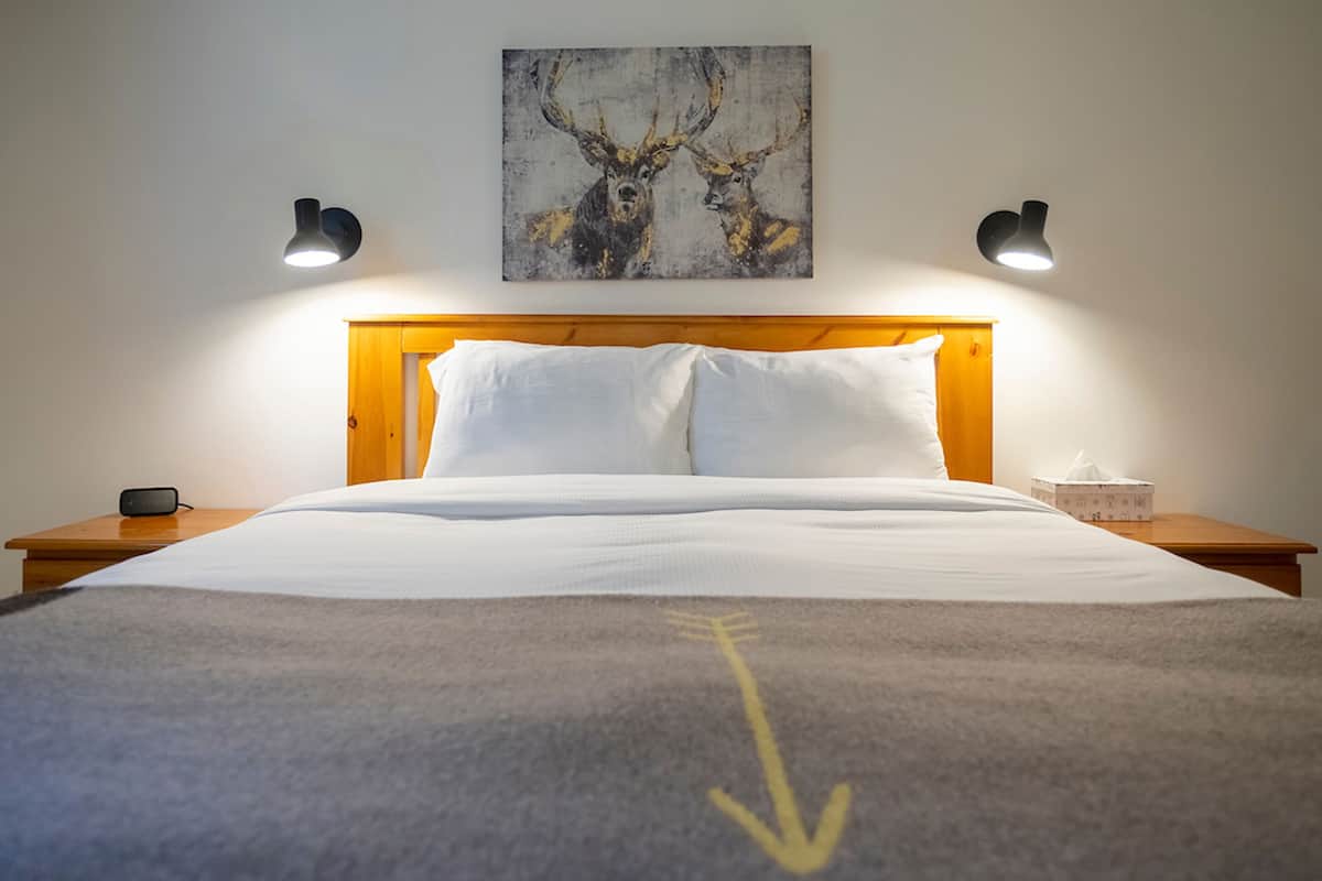Una cama bien hecha con sábanas blancas, un cabecero de madera y dos lámparas de noche.