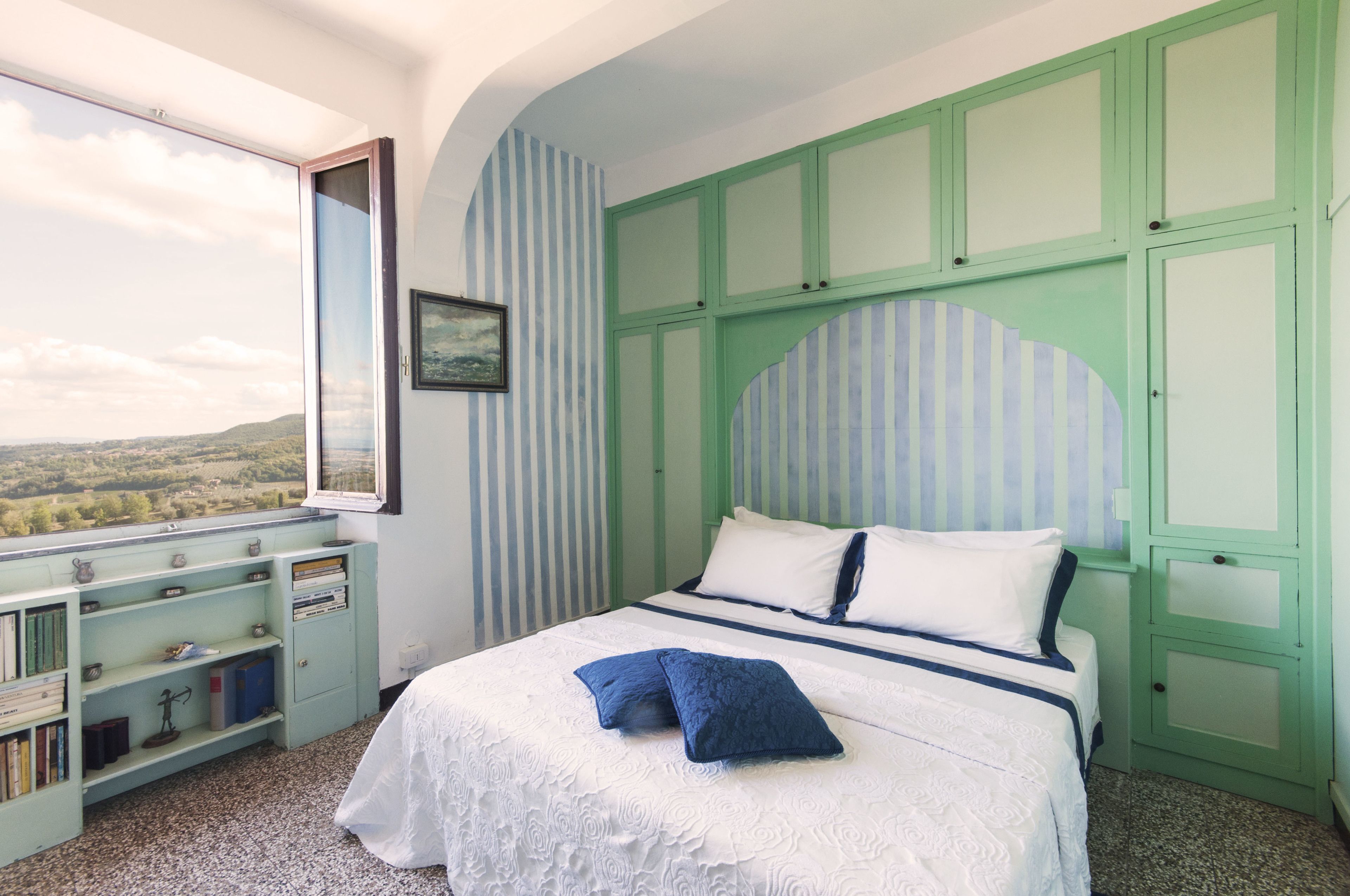 Een slaapkamer met een bed, een raam met uitzicht en een boekenkast.