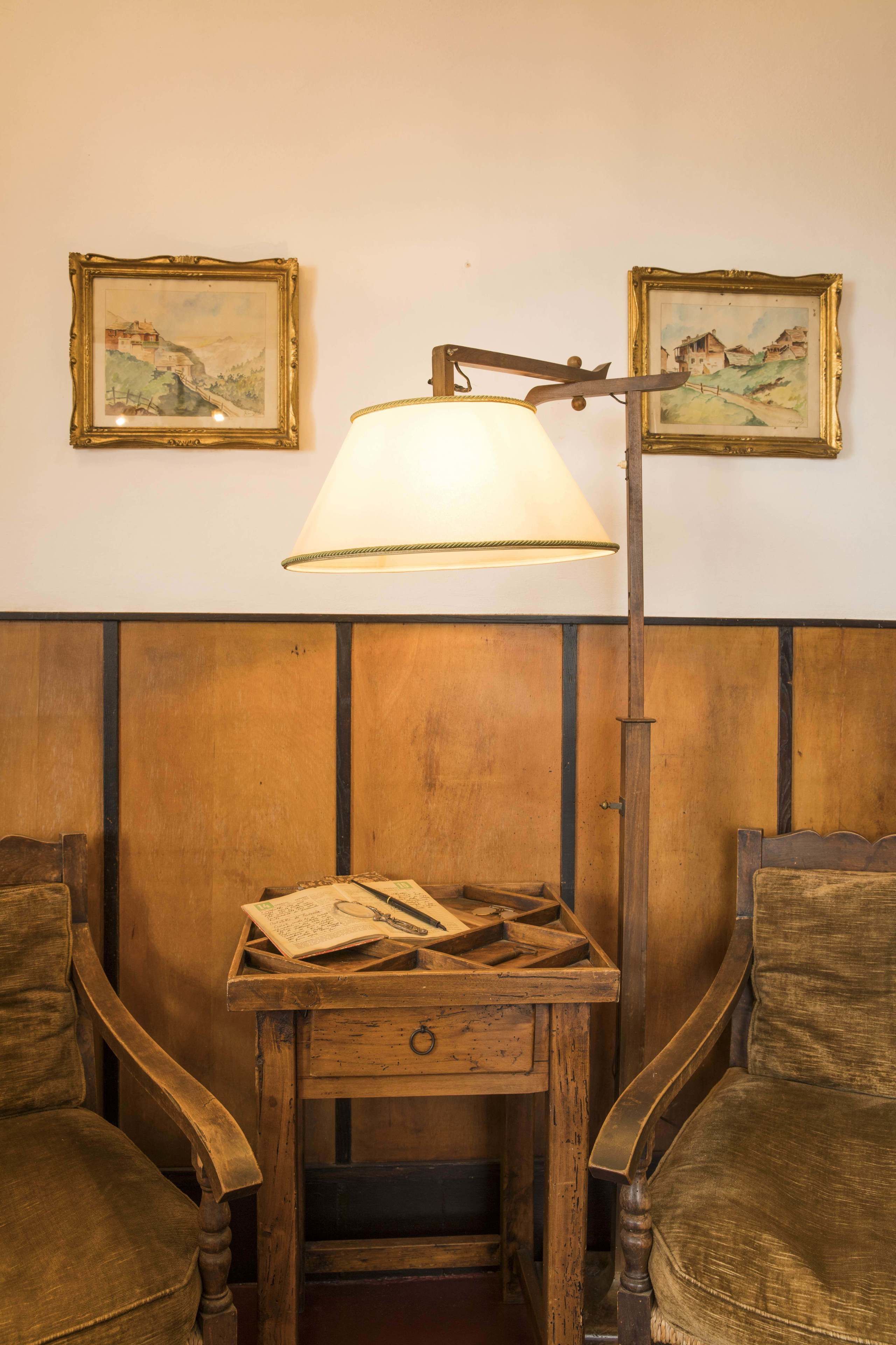 A wooden desk with a lamp, two chairs, and two framed paintings on the wall.