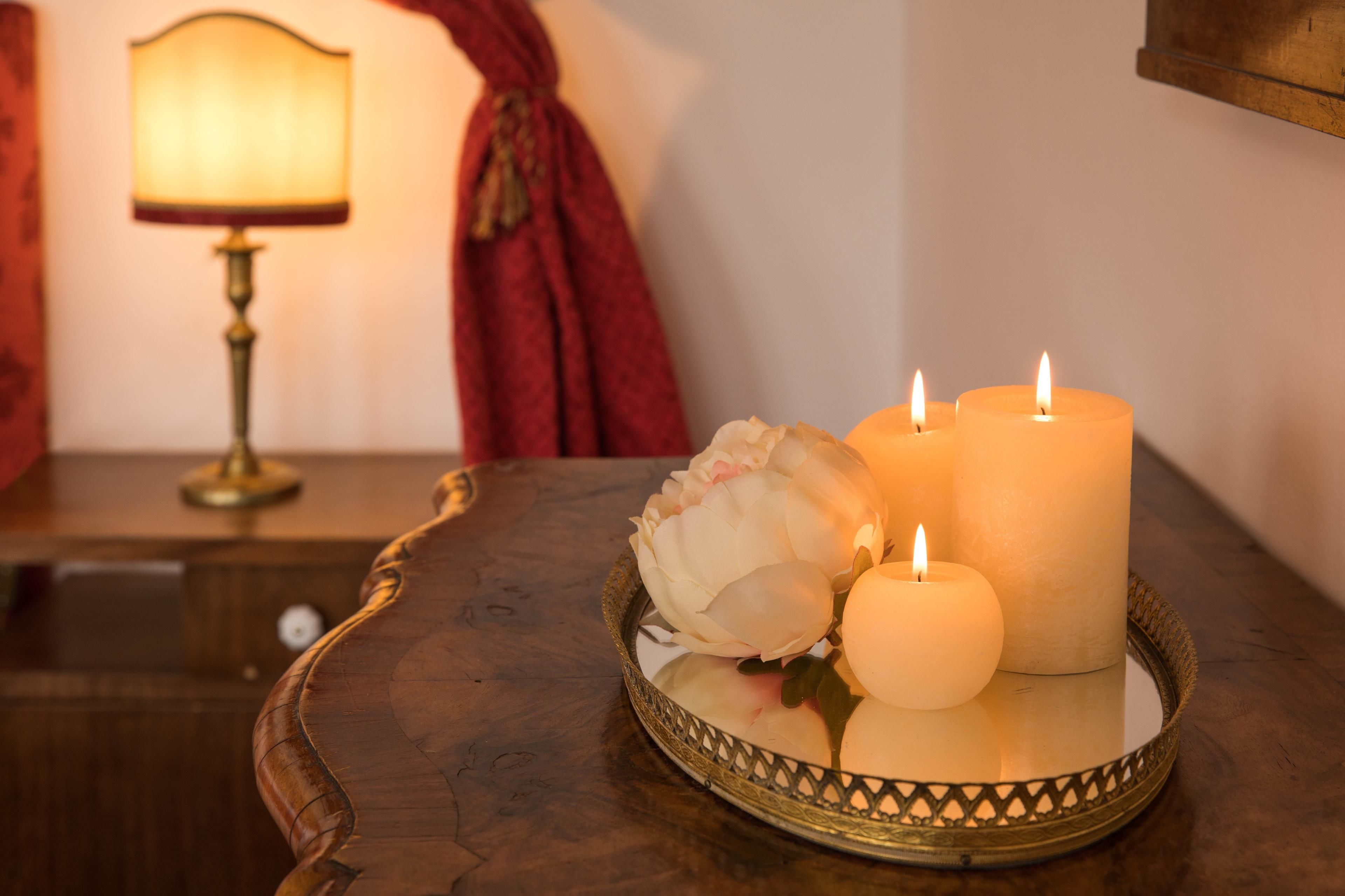A table with three lit candles and a white flower on a tray.