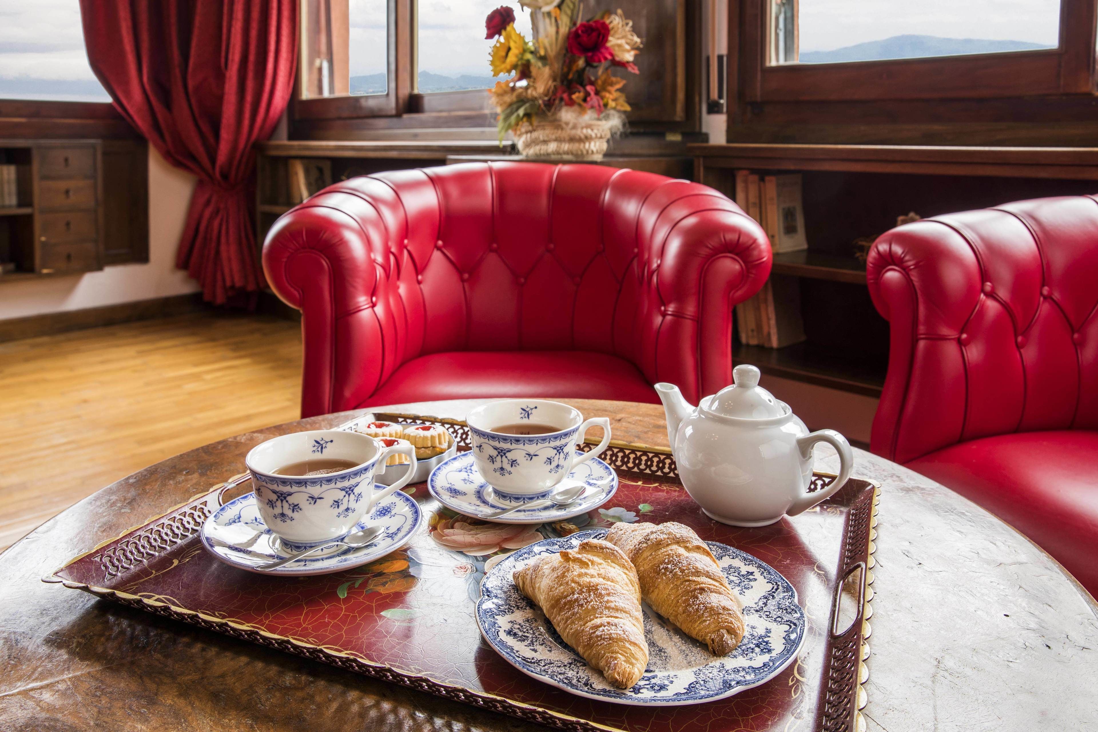 A dining table with a tray containing croissants, a teapot, cups, and a floral arrangement.