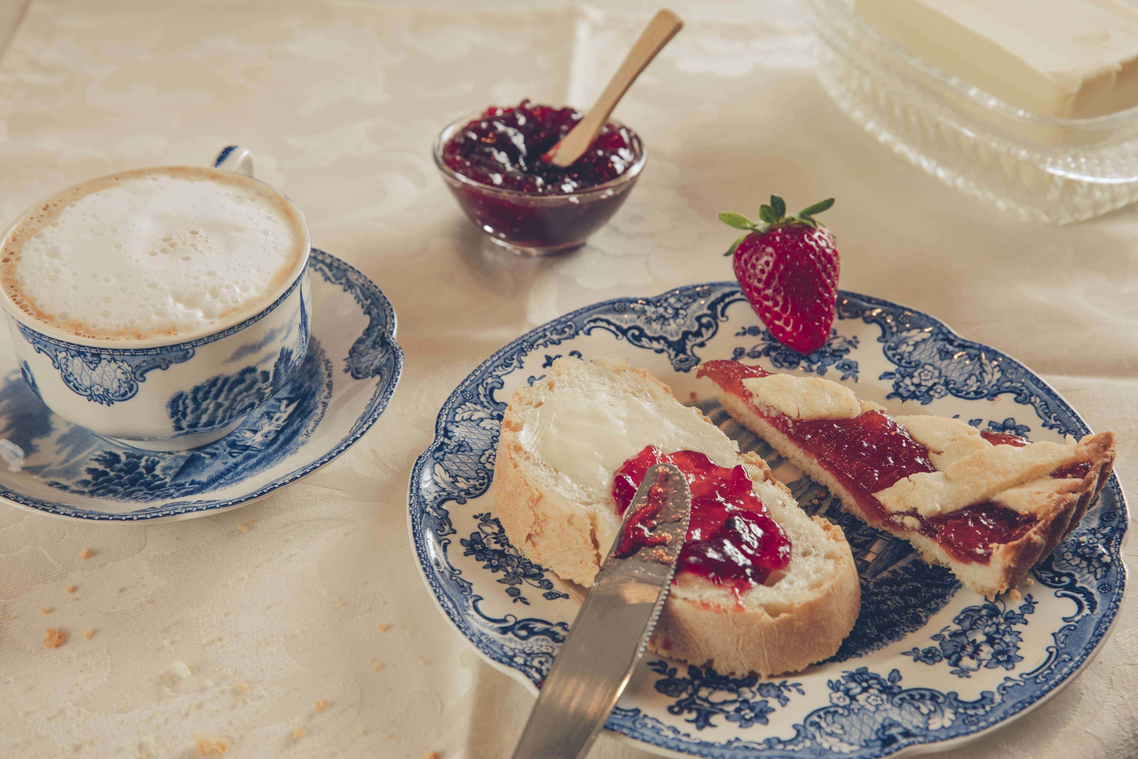 Une assiette avec une tranche de pain grillé garnie de confiture et d’une fraise, une tasse de café et un bol de confiture avec une cuillère.