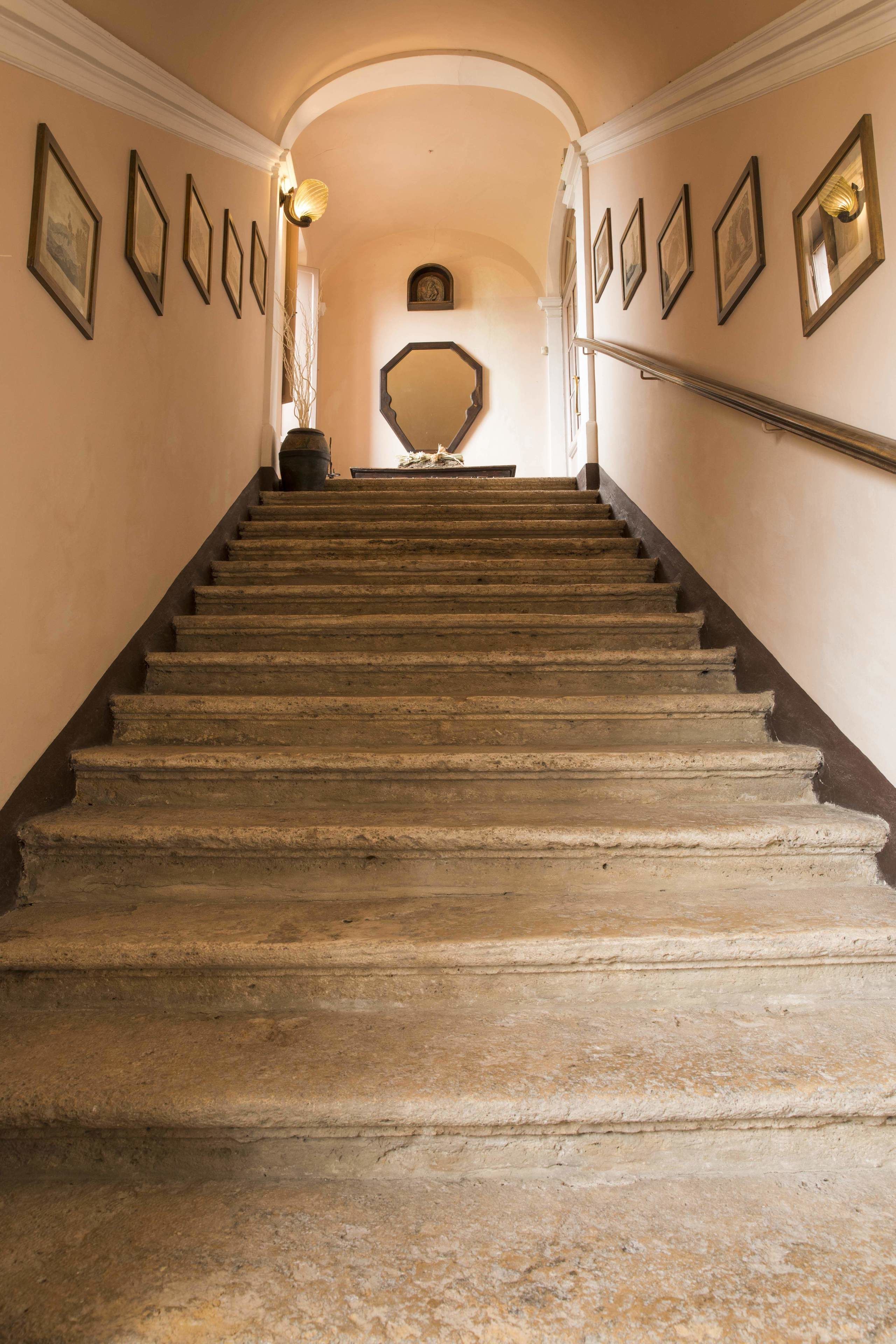 Un escalier en pierre avec une rampe, menant à un palier agrémenté d’un miroir et de tableaux encadrés accrochés aux murs.