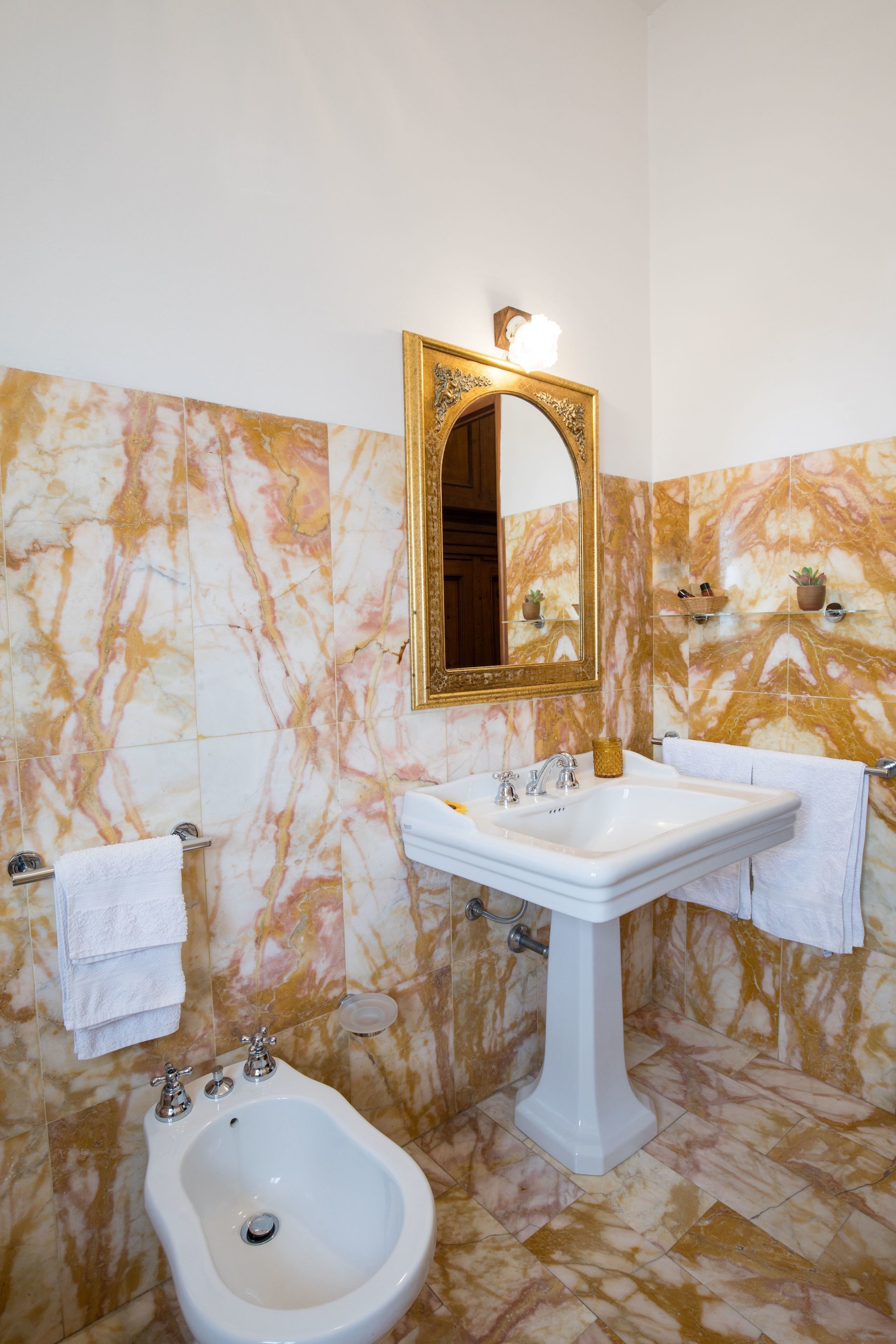 Ein Badezimmer mit einem Standwaschbecken, einem Bidet und einem großen Spiegel mit goldener Rahmung.