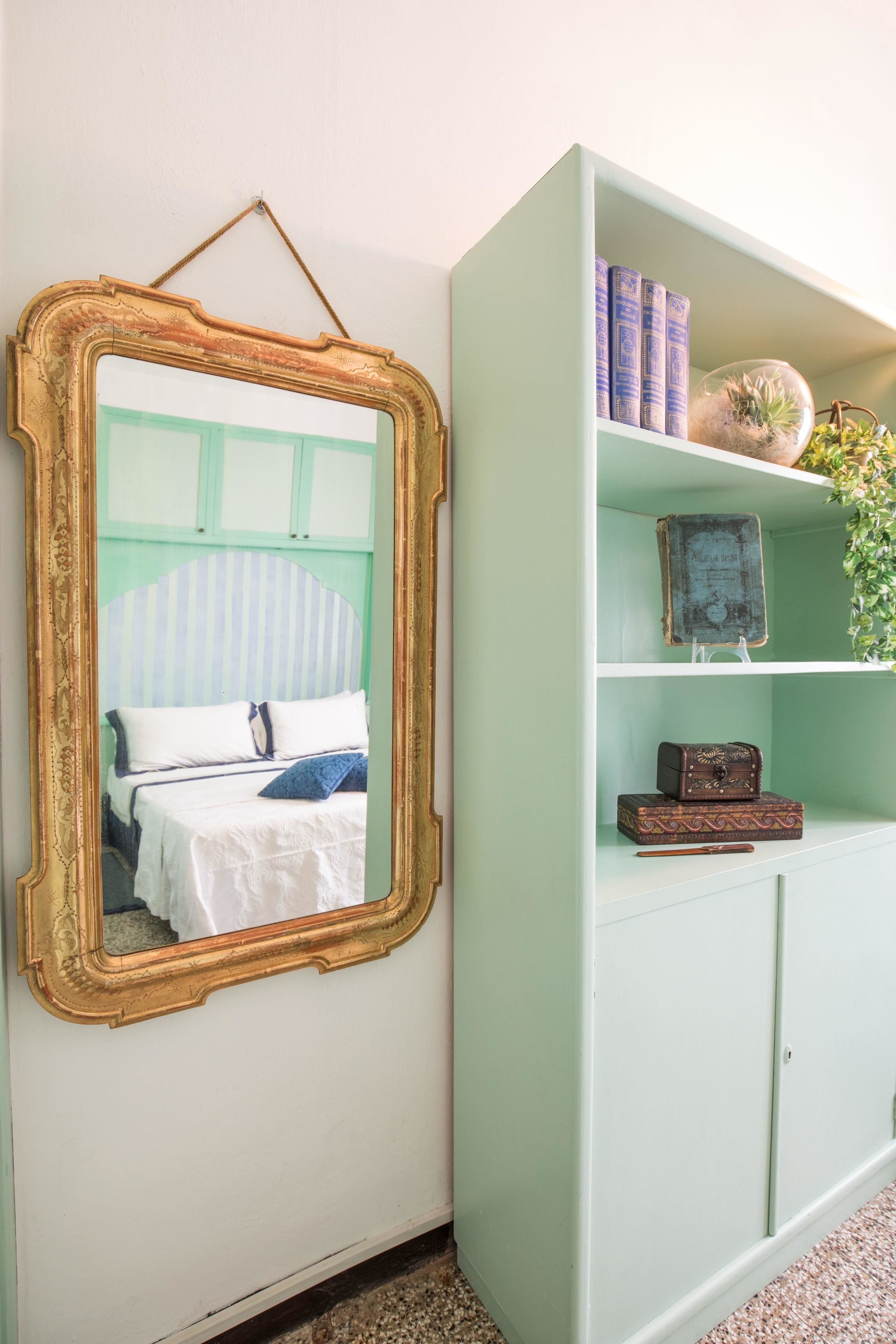Una habitación con una cama, un espejo y un aparador verde con libros y objetos decorativos.