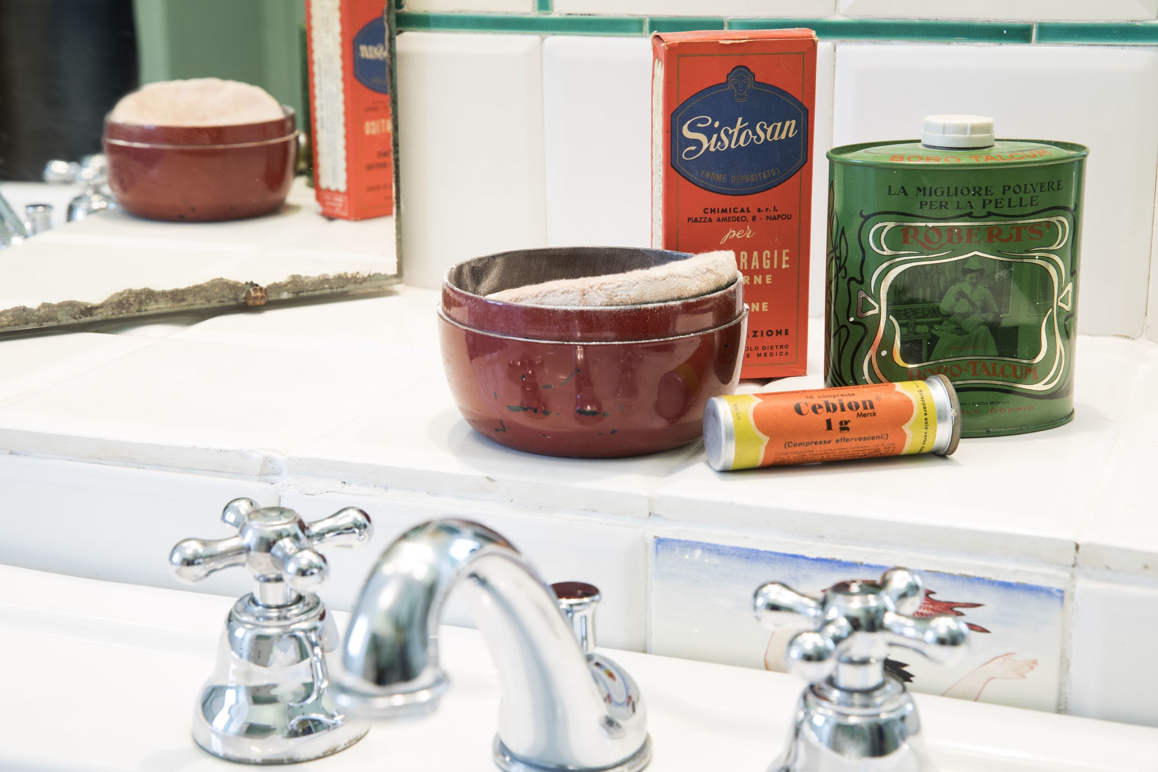 A bathroom sink with a mirror, a red bowl, a green canister, and a tube of toothpaste.