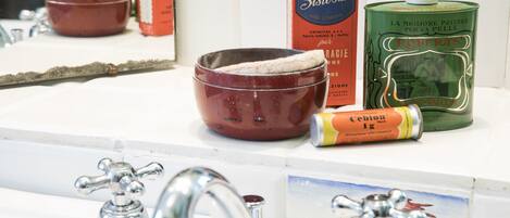 A bathroom sink with a mirror, a red bowl, a green canister, and a tube of toothpaste.