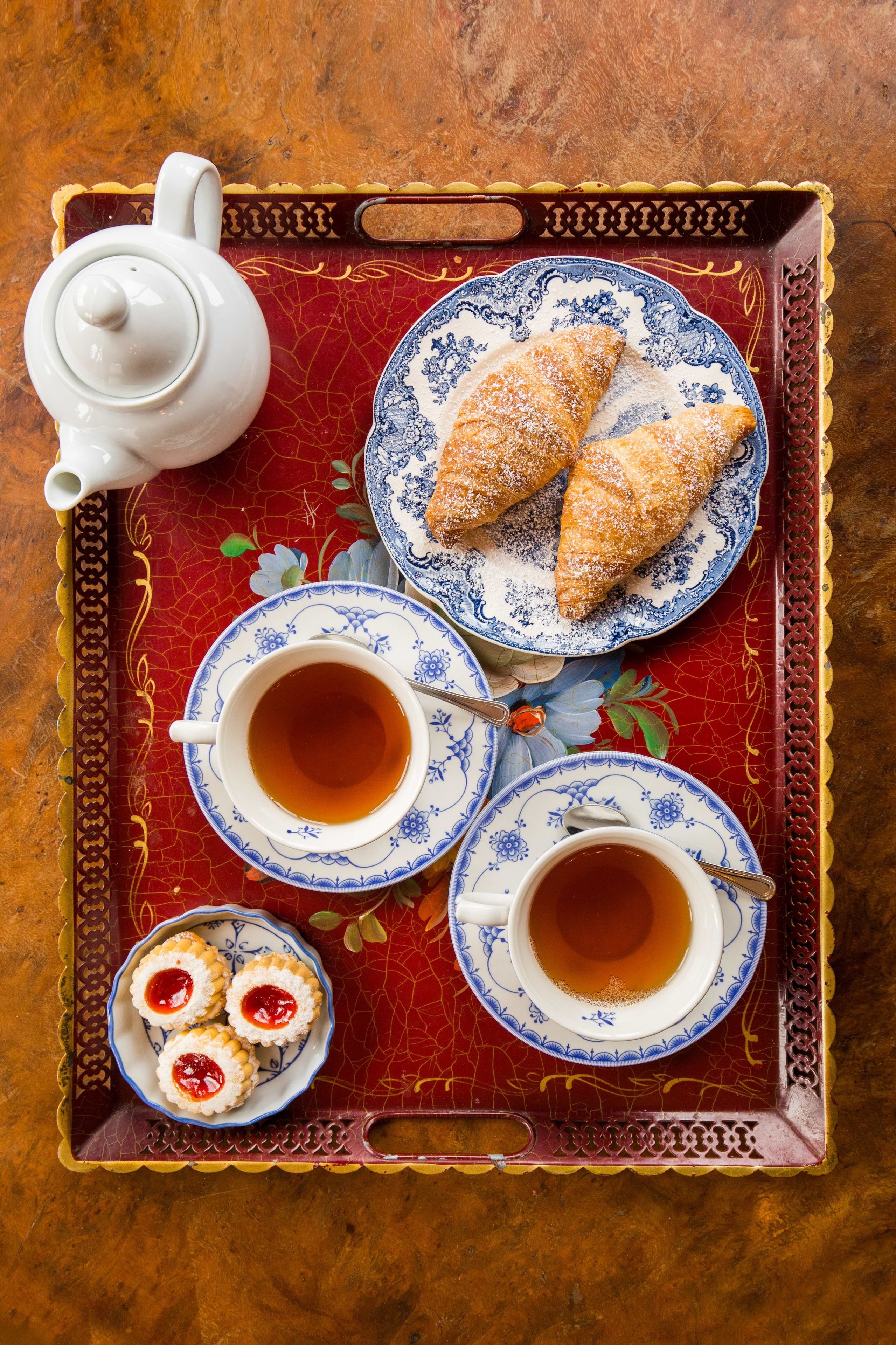 Un plateau avec une théière, deux tasses de thé, une assiette de pâtisseries et une assiette de biscuits.