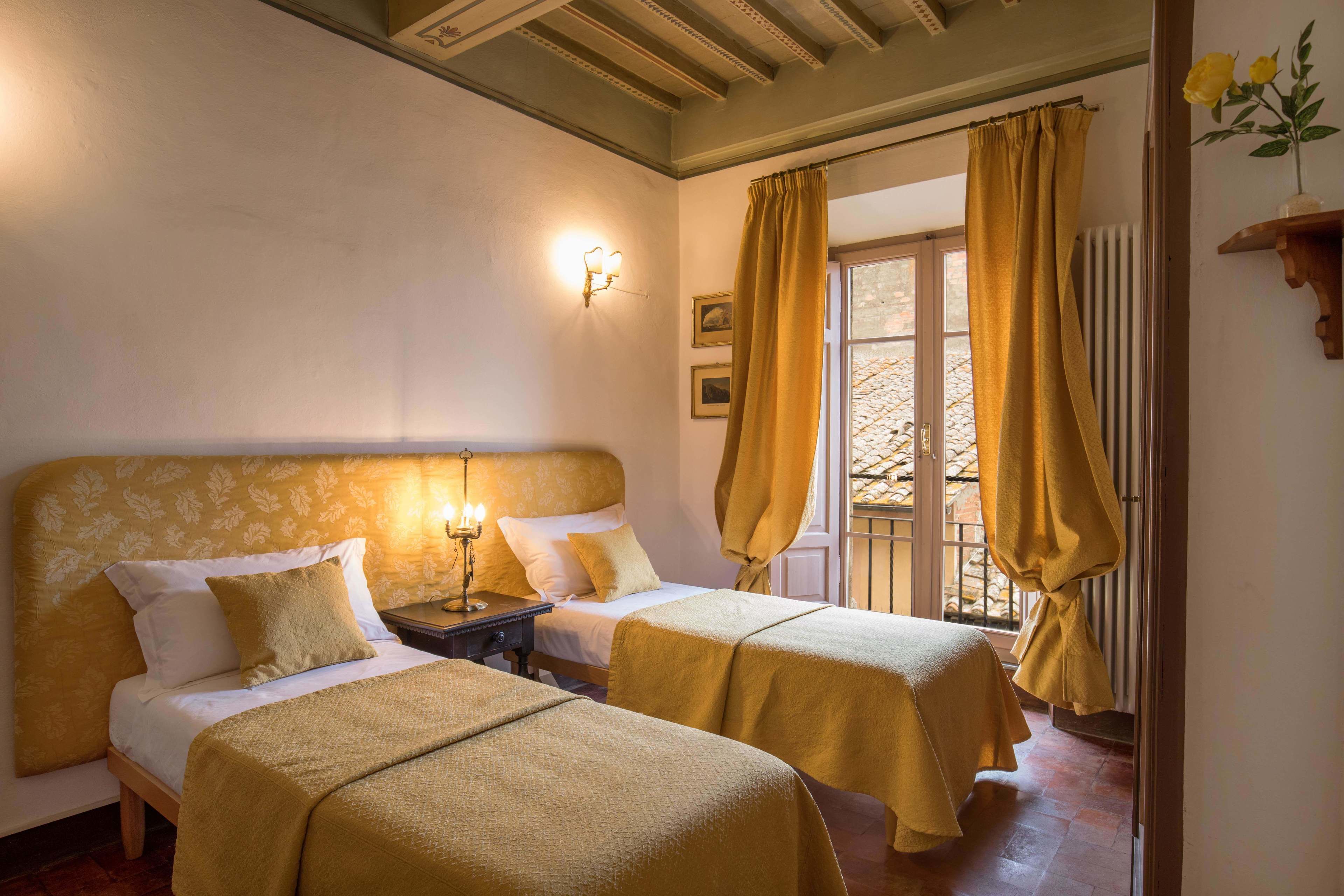 Une chambre avec deux lits, une table de chevet, une lampe fixée au mur et une fenêtre avec des rideaux.