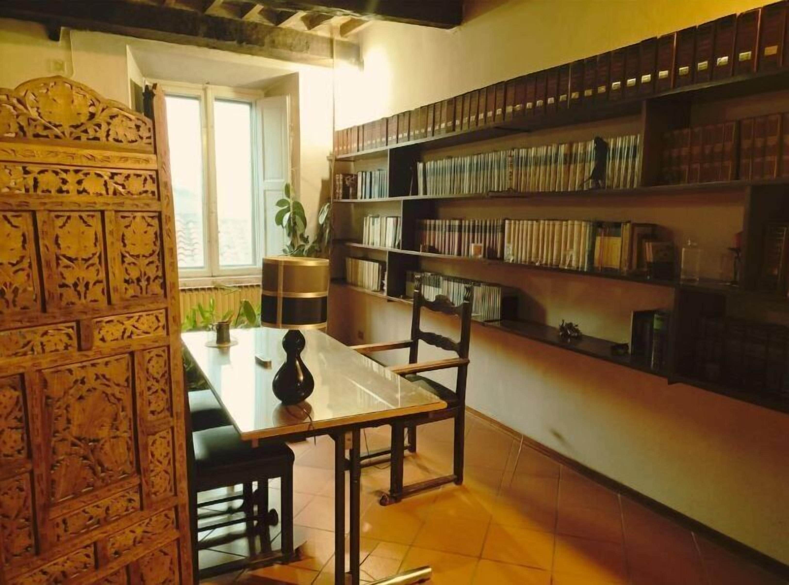 A room with a wooden table, chairs, a bookshelf, and a window.