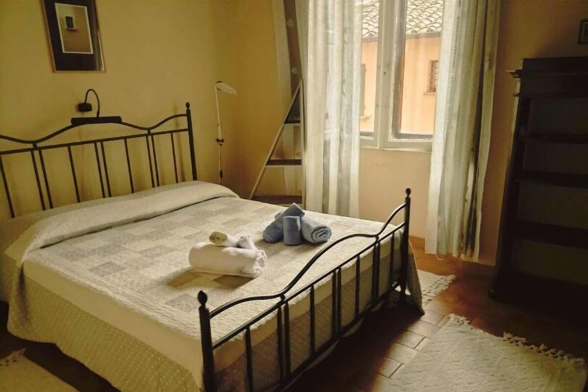Una cama con estructura metálica, una toalla enrollada y una toalla doblada sobre la cama.