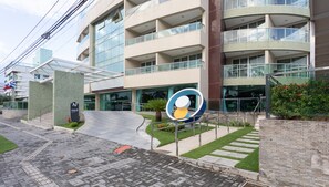 Um hotel moderno com fachada de vidro, várias varandas e uma área de entrada ajardinada.