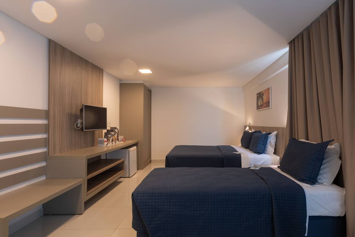 Habitación de hotel con dos camas, televisión, escritorio y una pequeña zona de estar.