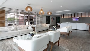 A modern living room with a white sofa, two white armchairs, a glass coffee table, and a TV mounted on the wall.