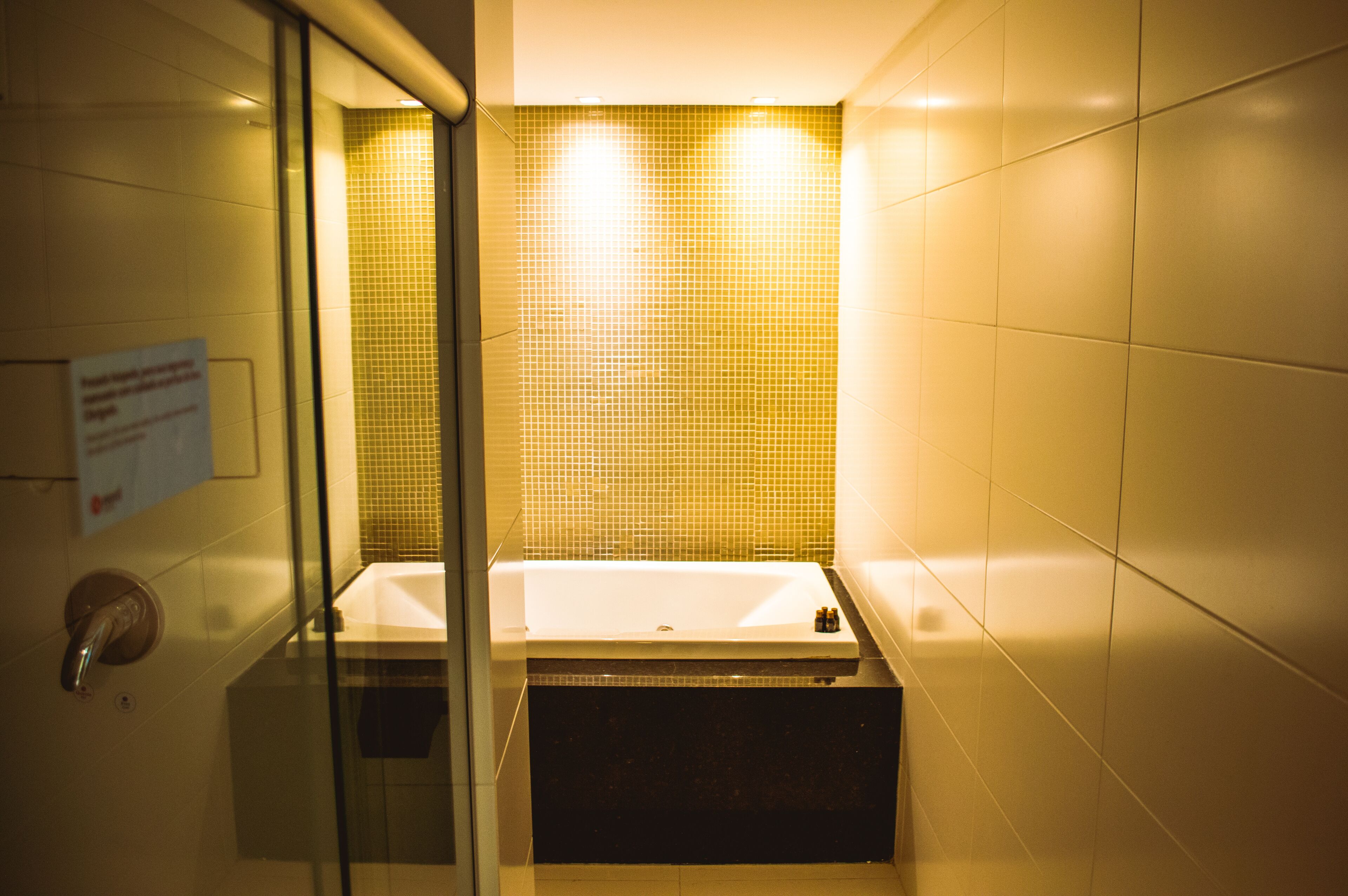 A bathroom with a glass partition, a white bathtub, and a yellow-tiled wall.