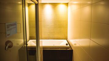 A bathroom with a glass partition, a white bathtub, and a yellow-tiled wall.