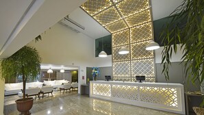 A modern reception area with a marble floor, white reception desk, and seating area with sofas and a potted plant.