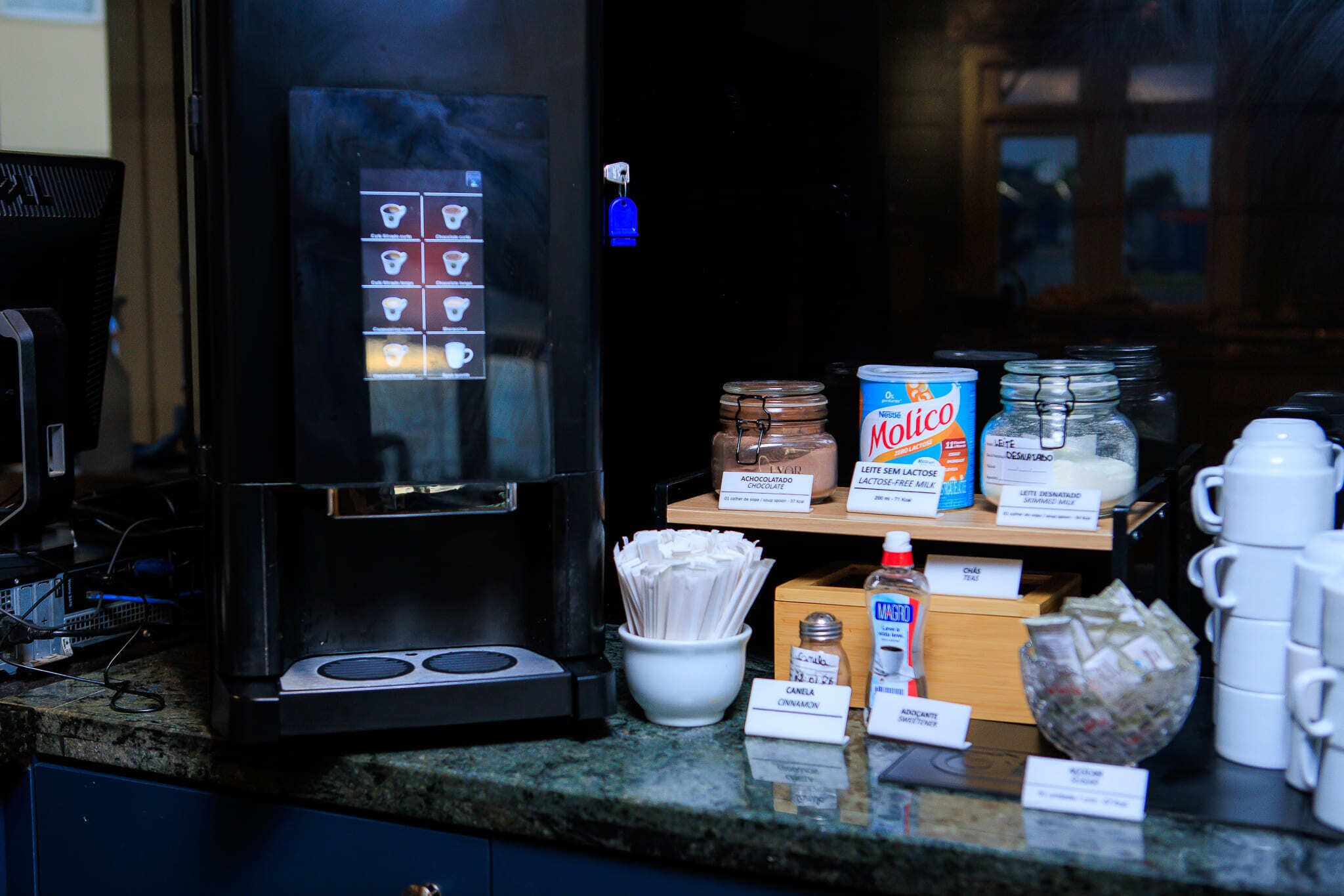 Una estación de café con una máquina de café, dispensadores de leche y crema, y recipientes etiquetados de crema para café.