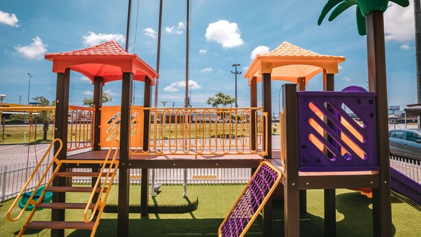 Un parque infantil con varias estructuras de juego, incluyendo toboganes y zonas de escalada, sobre césped artificial.