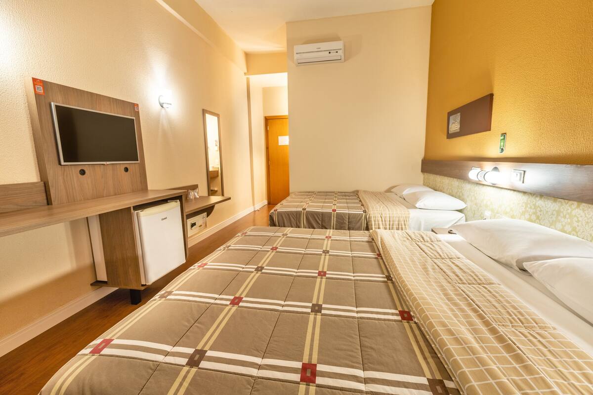 A hotel room with two beds, a TV, a mini-fridge, and a mirror.