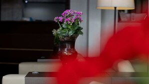 Un moderno vestíbulo de hotel con un jarrón de flores moradas sobre una mesa, un sofá y una lámpara.